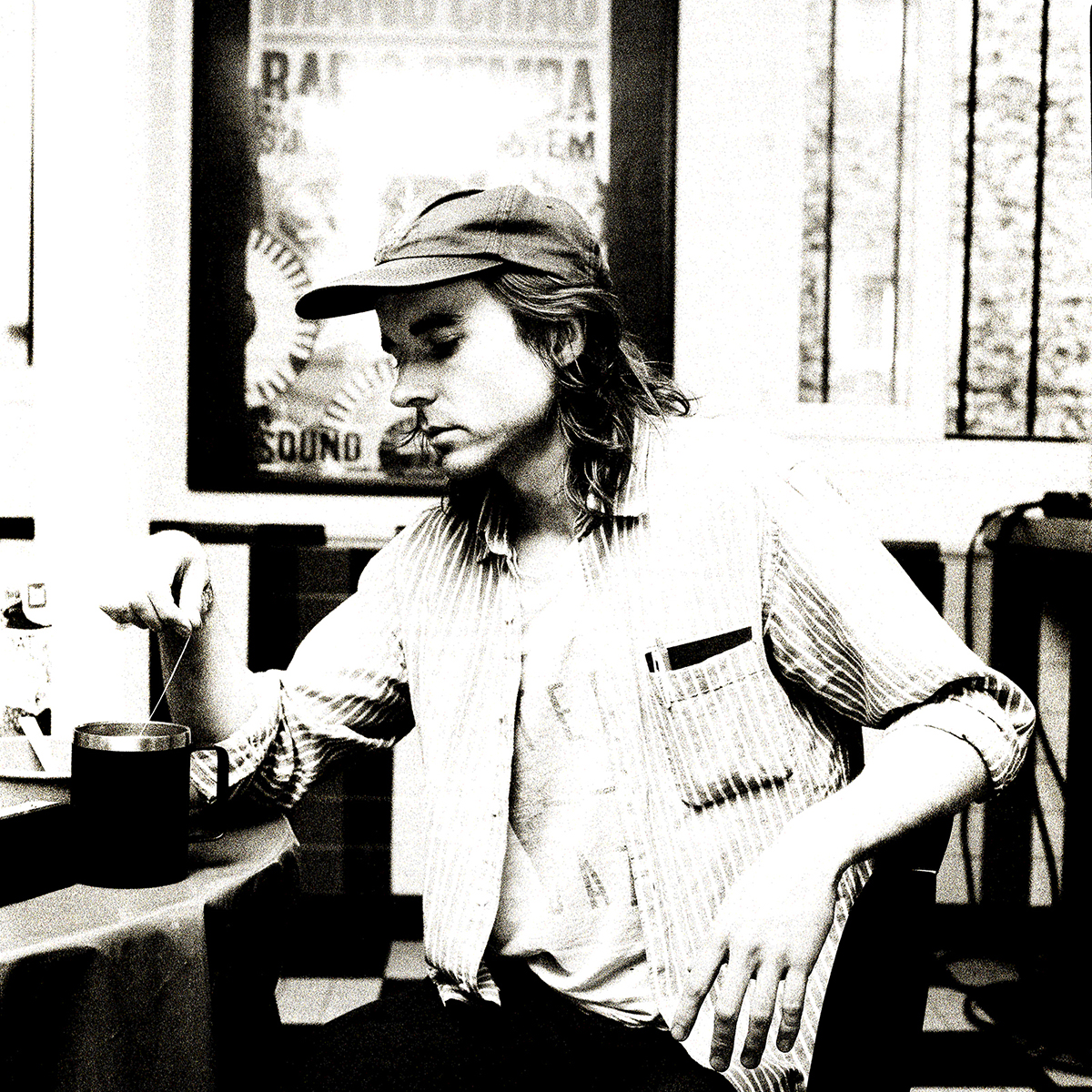Slightly grainly black and white photo of singer-songwriter Any Shauf seated at a table, tugging at a tea bag in a mug